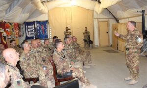 persona in divisa militare spiega in piedi spiega a gruppo di militari in mimetica seduti