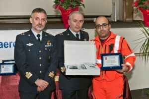 foto comandanti AM con persona in divisa rossa che regge una targa